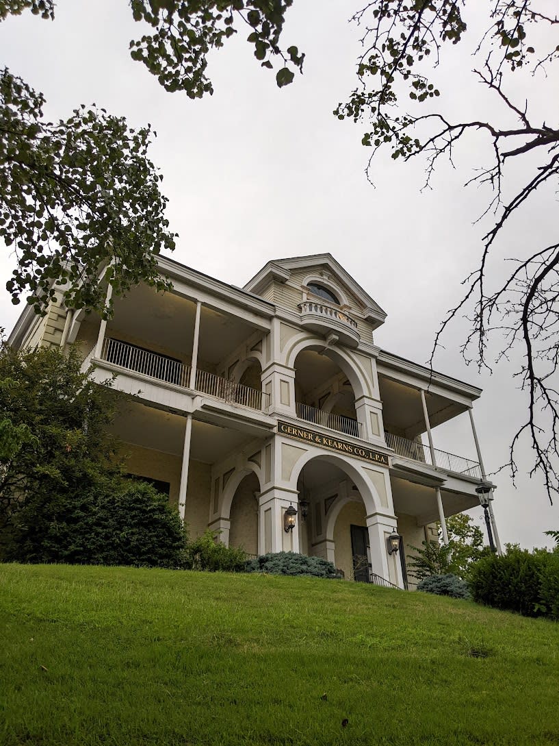 The image is of the Taylor Mansion which is a federal style, white mansion with grass and tree's surrounding it.