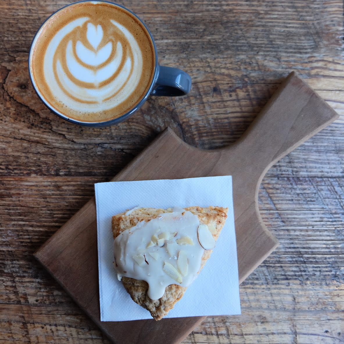 Image is of a late' that has a fern design and a scone with icing and almonds.