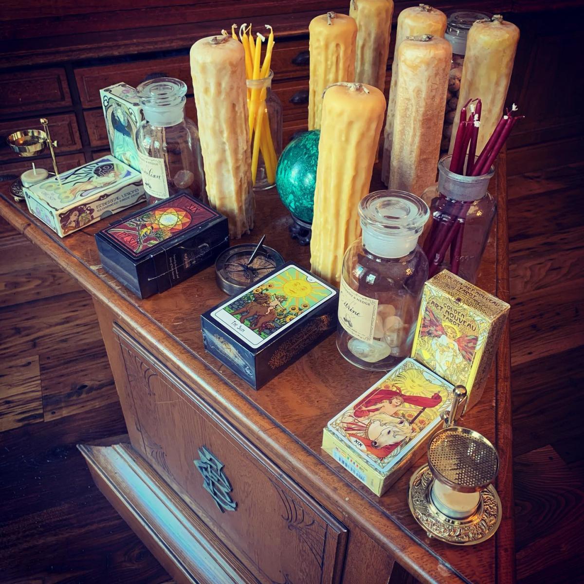 Image is of inside Hierophany & Hedge. There is a triangle table and it is holding candles, tarot decks and stones.