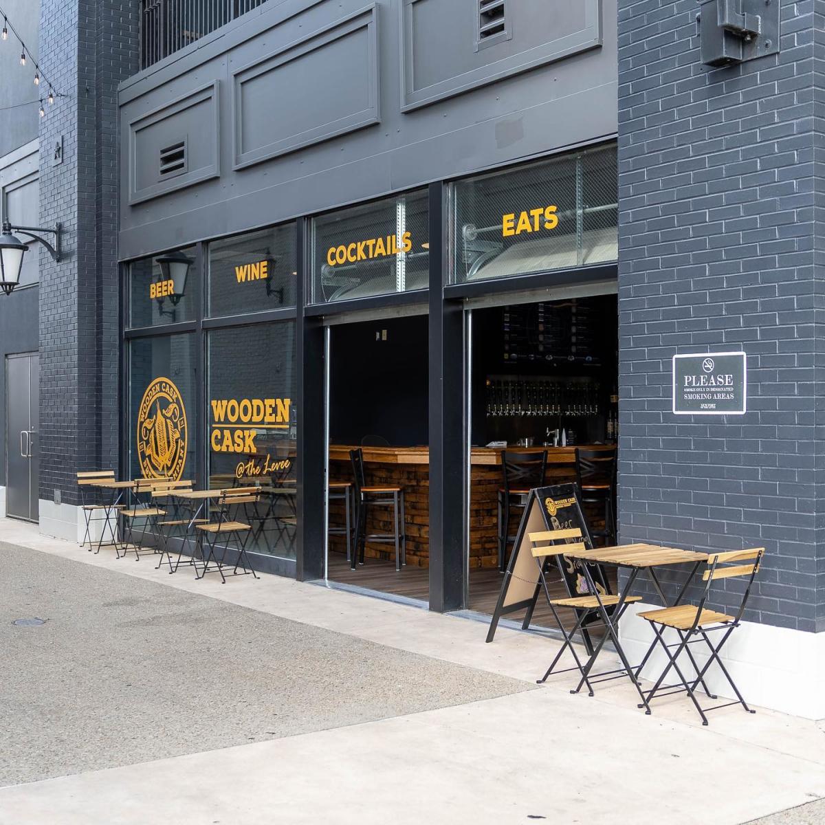 Image is of the front of the Wooden Cask tap room in the Levee with 3 small table and chairs up against the wall.