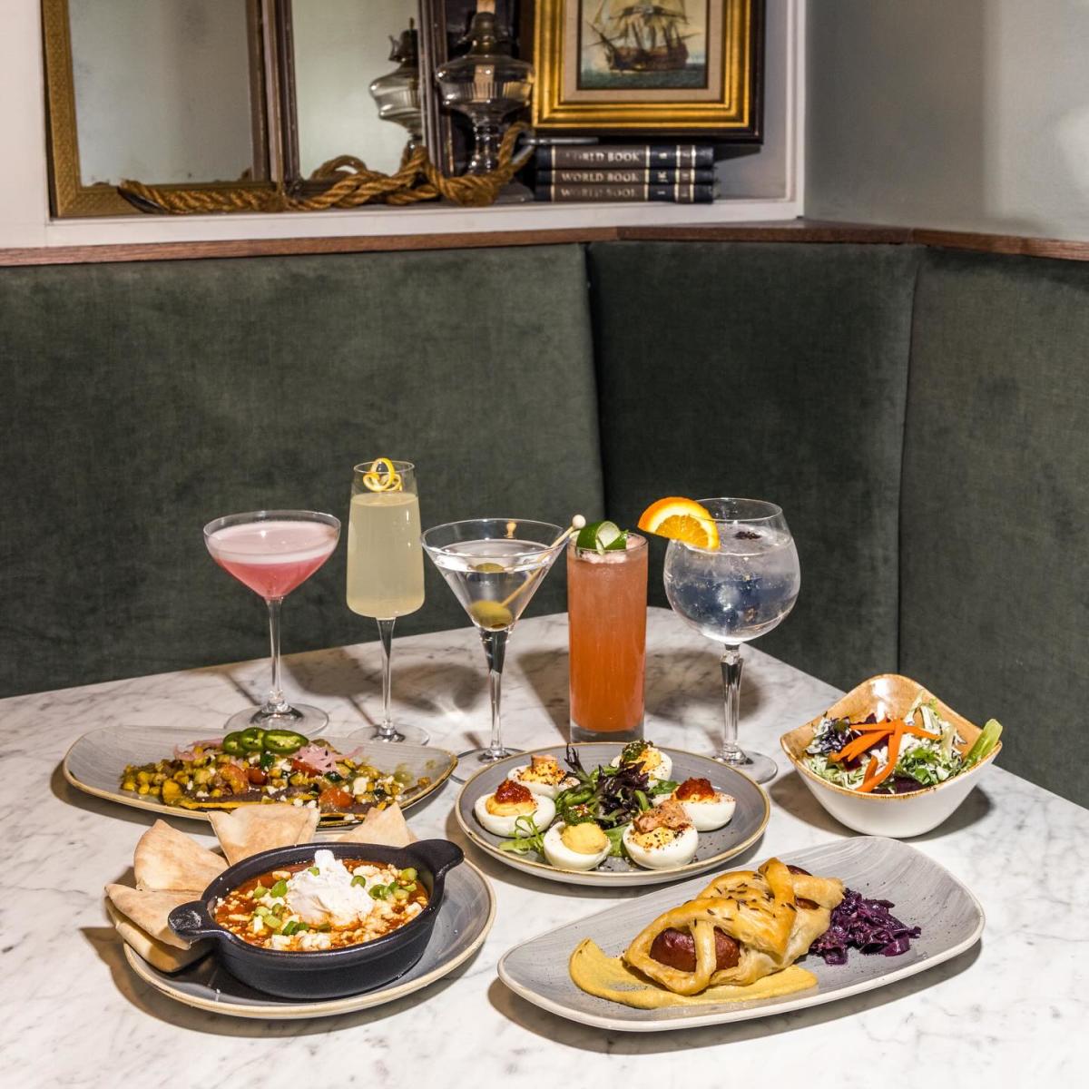 A table with several tapas plates and cocktails.