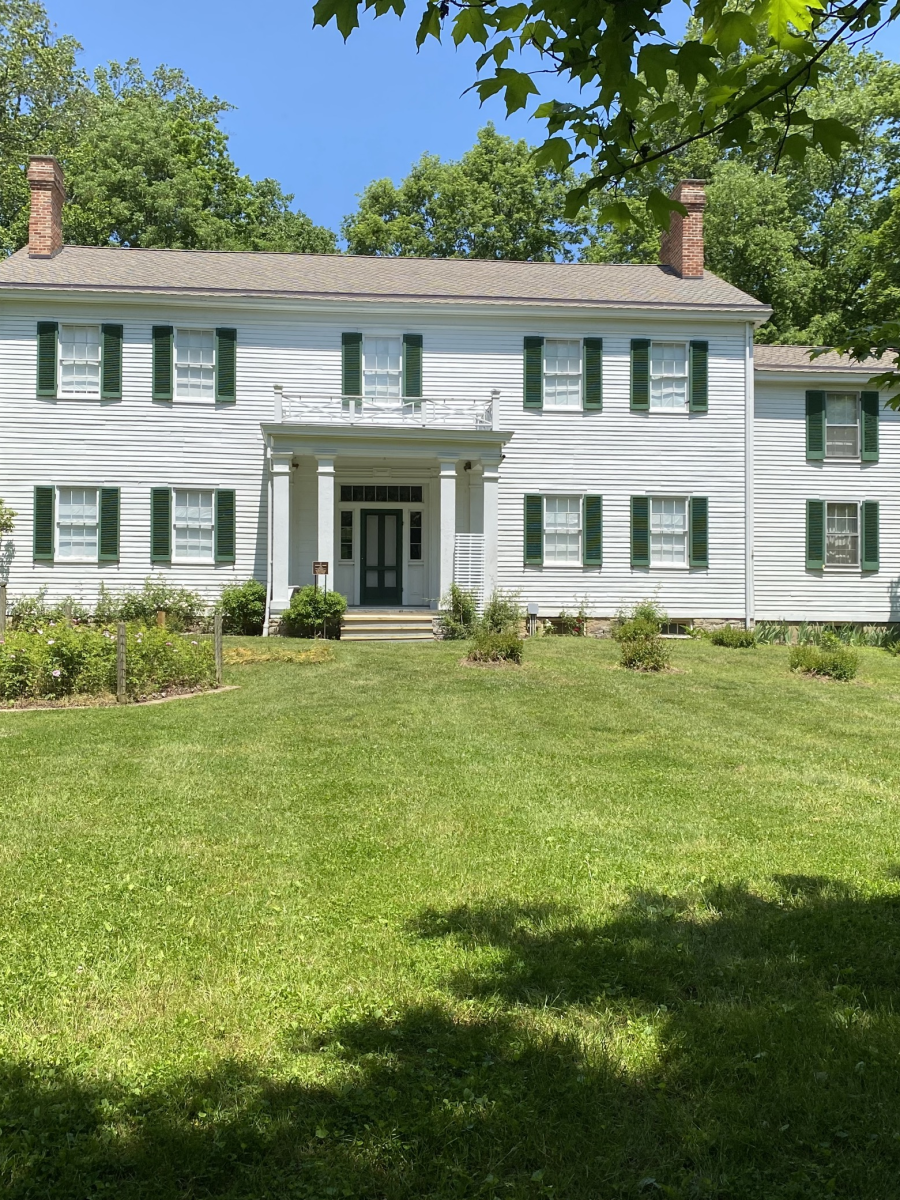 Image is of the Dinsmore Homestead house during the summer with trees in bloom on a bright and sunny day.