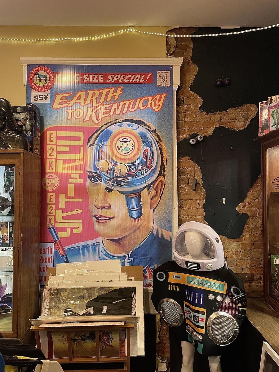 Image is of a poster that says "Earth to Kentucky" with a man whose brain looks like a robots.