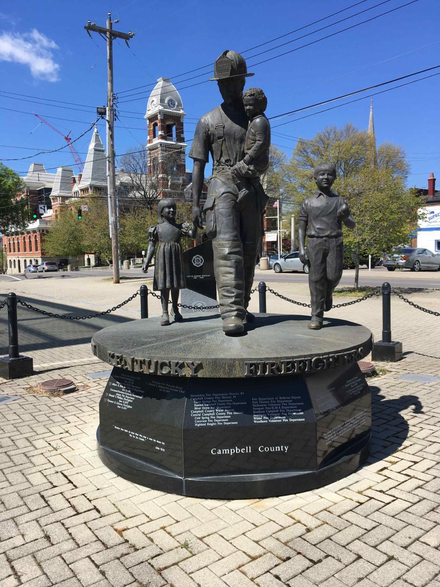 A statue of a Newport Kentucky firefighter holding a child and holding the hand of another as he leads a third child to safety
