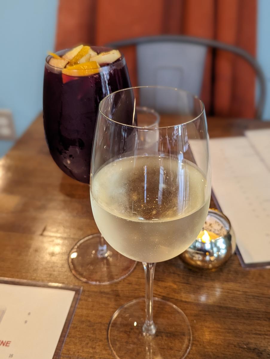 Image is of a glass of chilled white wine in front with a glass of red sangria behind it, topped with fruit.