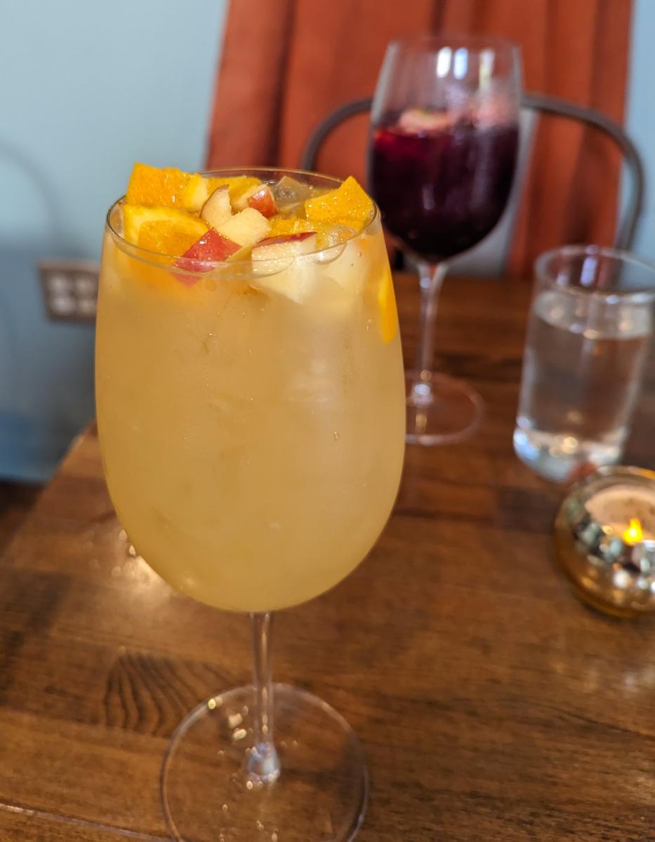Image is of a white sangria with fruit in the front and a glass of red sangria in the back with fruit.