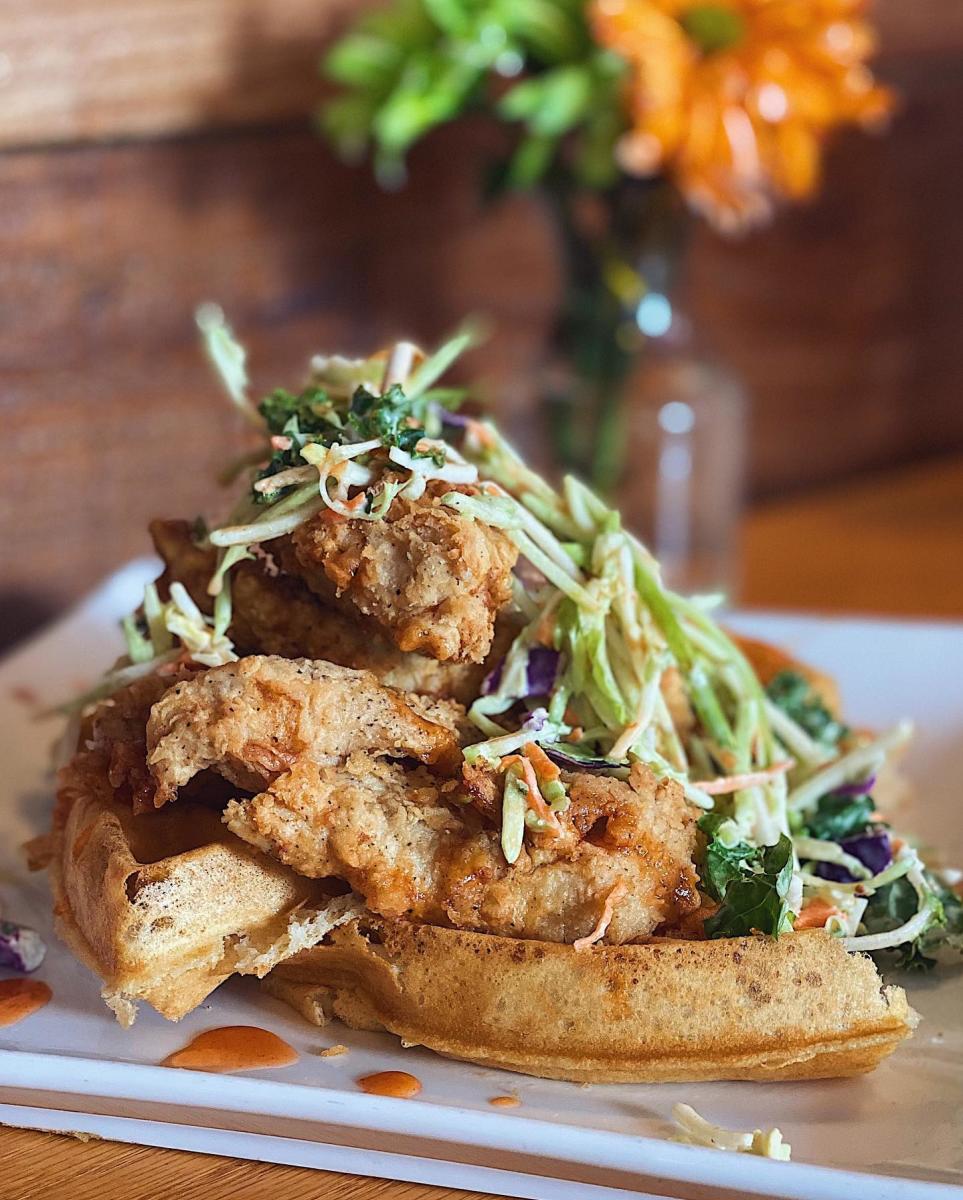 Image is of a golden waffle with fried chicken on top and coleslaw..