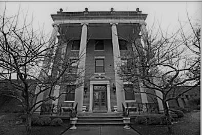 A foreboding building sits against a grey sky with spindly trees in front.