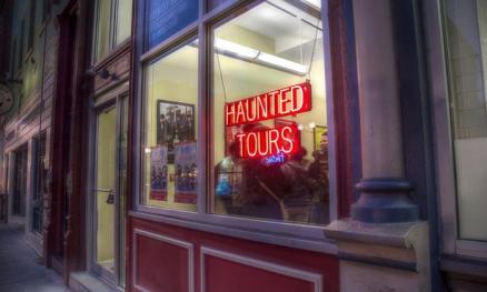 A neon sign glows red in a store front window. The sign says "Haunted Tours"