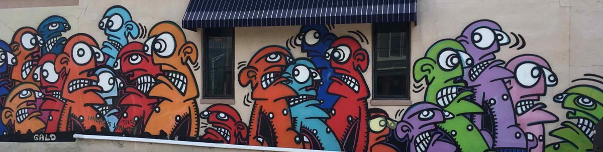 Street art in Covington, Ky. depicting multi-colored faces with big eyes by artist Galo.