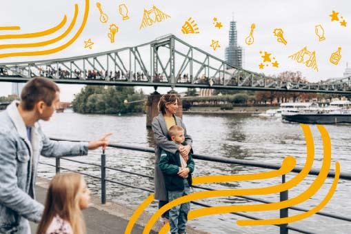 A family looks at the river with a bridge in the background.