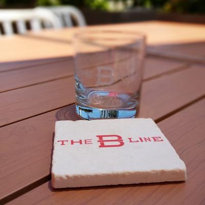 A marble coaster with "The B Line" printed on it sits in front of an empty rocks glass etched with "The B Line".