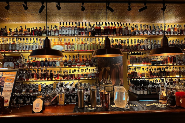 A backlit bar full of different bottles of bourbon