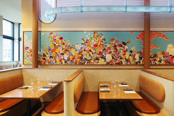 Cozy booths with tables set for dining are in the foreground, while a vibrant, colorful mural fills the background wall.