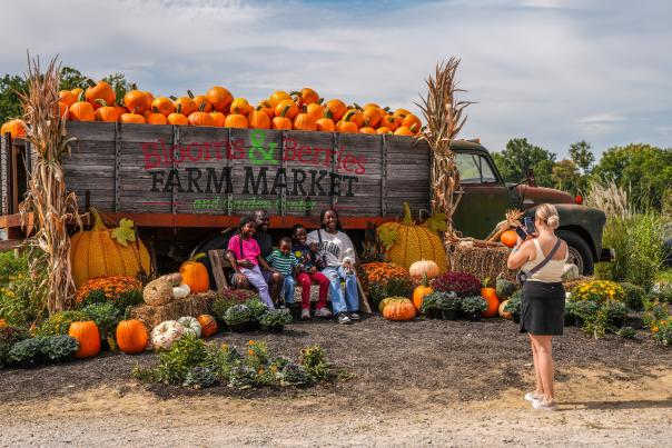 A group poses for a photo in front of a truck full of pumpkins at a fall festival