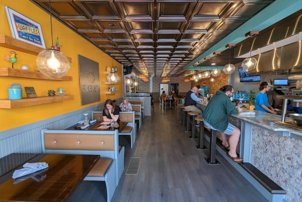 Image is of inside the Pike Street restaurant where you can see the kitchen and grill on the right side and booths on the left side in a shot gun style building.