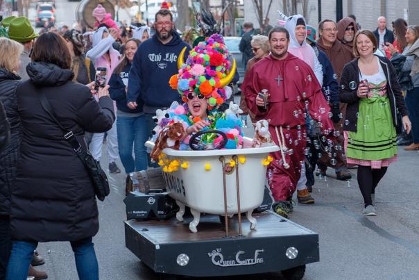 A woman sits in a bathtub during the Bockfest parade wearing a colorful pompom hat
