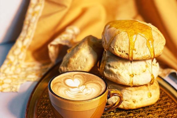 A golden-brown tray with three golden hued biscuits with honey drizzeled over it, sitting next to a brown and tan coffee mug with a late.