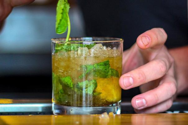 A man's hand adds a spring of mint to a cocktail glass with a mint julep on ice