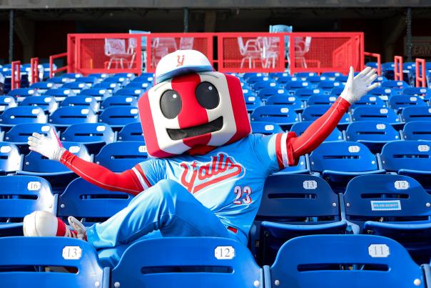 An anthropomorphic version of the famous red and white striped Florence, KY watertower, dressed in a blue and red Florence Y'alls uniform. It sits in the stadium seats arms stretched wide.