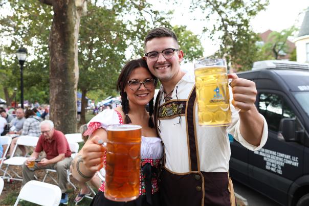 A smiling couple hoist beer steins to the camera.
