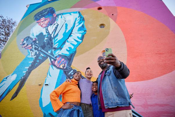 A family takes a selfie in front of the Mr. Dynamite James Brown mural in OTR