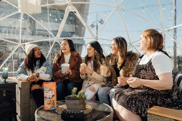 Image is of 5 women sitting in a clear igloo, laughing and having fun.