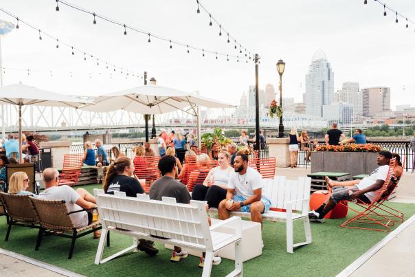 A group of people enjoy outside at Bridgeview Box Park. The Cincy skyline is in the background.