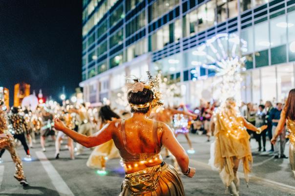People dressed in white lights and sparkling dance as they move away from the camera down the street.