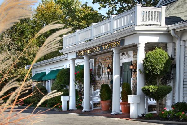 Exterior of Greyhound Tavern entrance. White columns flank the porch dotted with green bushes.