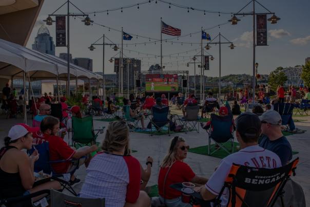 People sitting in lawn chairs wearing Red's gear watching the Red's play on an outside projection screen.