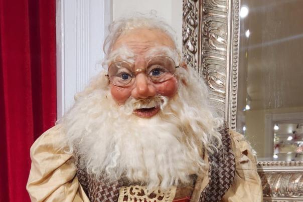 A vintage Santa figuring with white beard and wire-rimmed glasses sits on a fireplace mantle