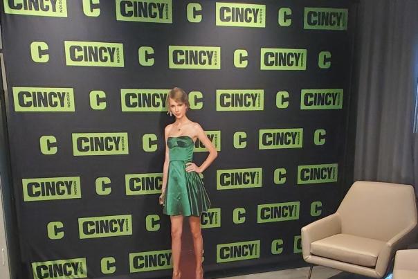 A cardboard cut-out of Taylor Swift stands in front of a branded Cincy Region backdrop for people to take photos with