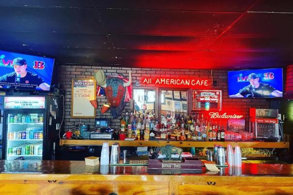 A red neon sign reading "All American Cafe" sits behind the wooden bar of Larry's in Covington