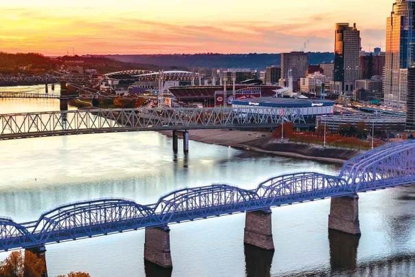 Image is an arial view of the Purple People Bridge spanning the Ohio River, connecting Newport, KY to Cincinnati, OH.
