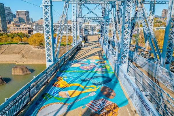 An aerial view of the Purple People Bridge mural "Where We Connect" featuring attributes unique to the Cincy Region, like beer, bourbon and Cincinnati-style chili