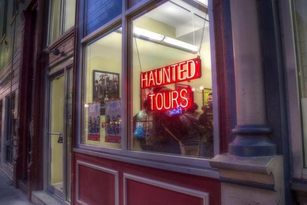 A neon sign glows red in a store front window. The sign says "Haunted Tours"