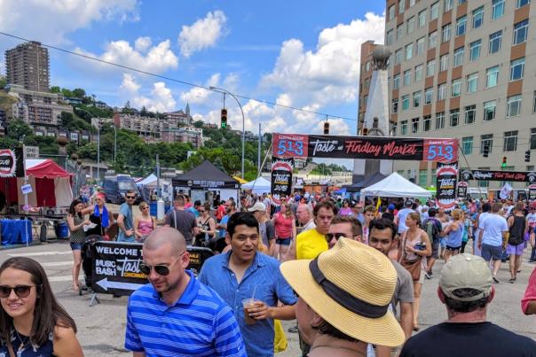 Taste of Cincinnati crowd in downtown Cincy headed under banner with blue sky and Mt. Adams in background