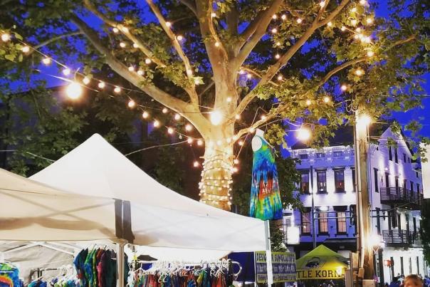 A tree strung with white lights shining down on colorful booths at a street festival in Mainstrasse Village