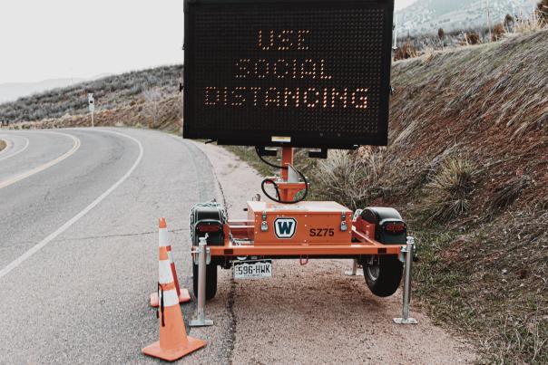 A light up road sign that says Use Social Distancing on the side of a highway