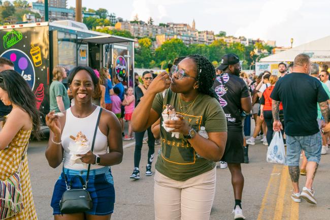 Two women enjoy food at Taste of Cincinnati, with Mt. Adams in the background.