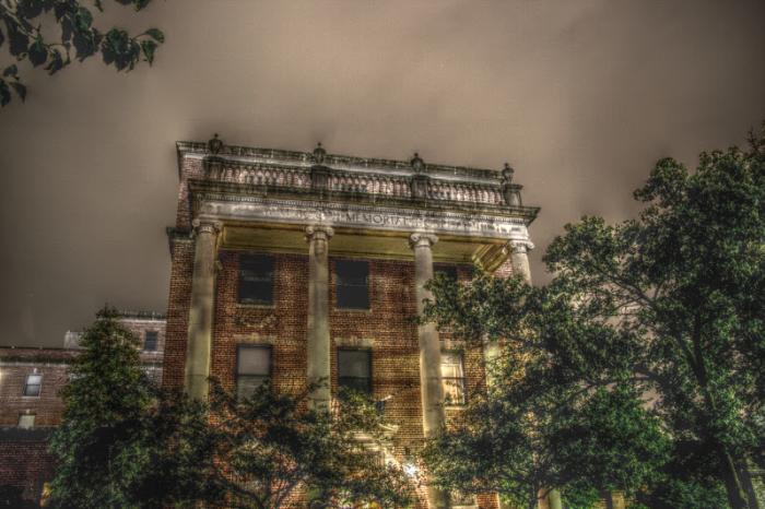 An eerie photo of a large building with columns on the front. It's flanked by trees.