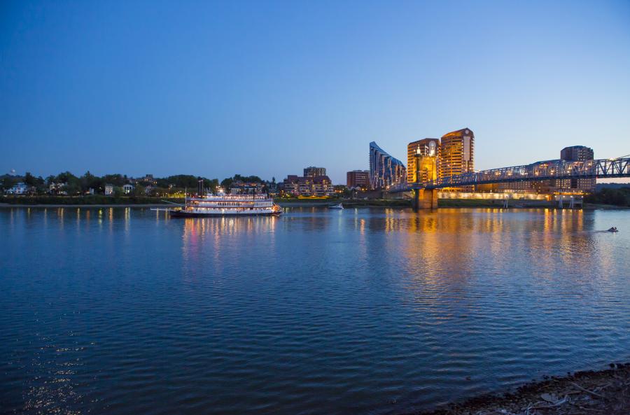 BB Riverboat is lit up for an evening cruise. The Roebling Bridge is illuminated. The Ohio River is dark and still.