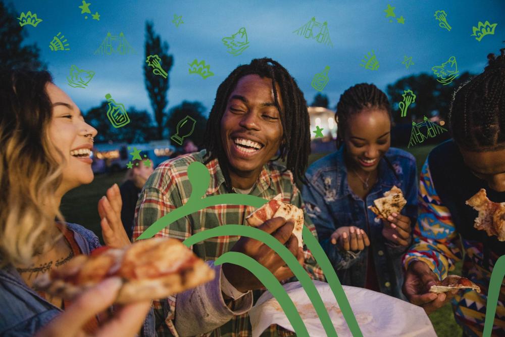 A group of people share a meal together. Green, hand drawn elements decorate the photo.