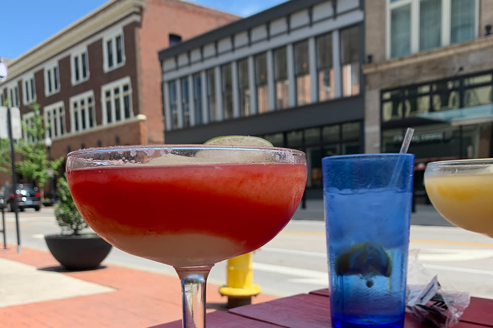 A red margarita sits on a red patio table along a downtown street