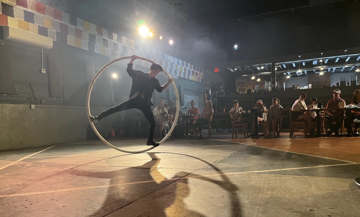 Image is of a circus performer in a German Wheel in front of an audience.