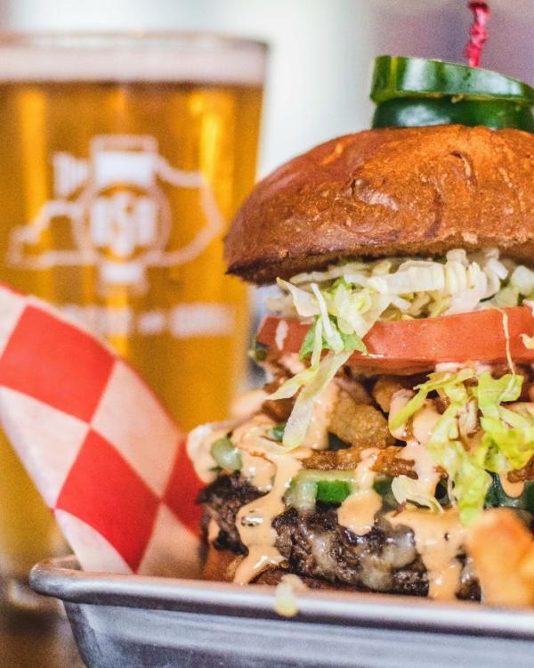 tall burger with a glass of beer behind it at 859 taproom and grill in florence ky
