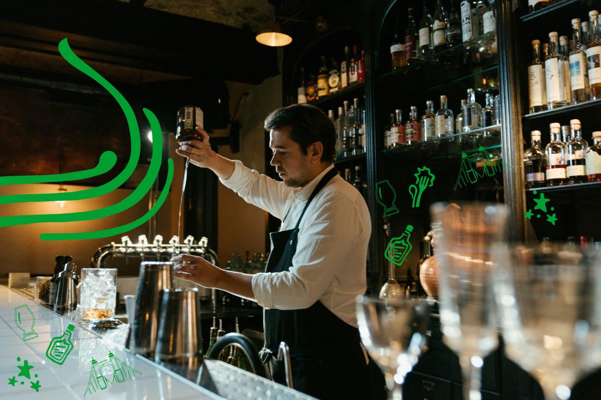 A bartender standing in front of shelves of liquor creates a cocktail.