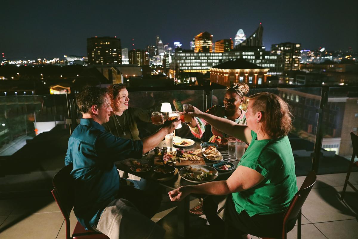Four people toast each other at night with the Cincinnati skyline in the background