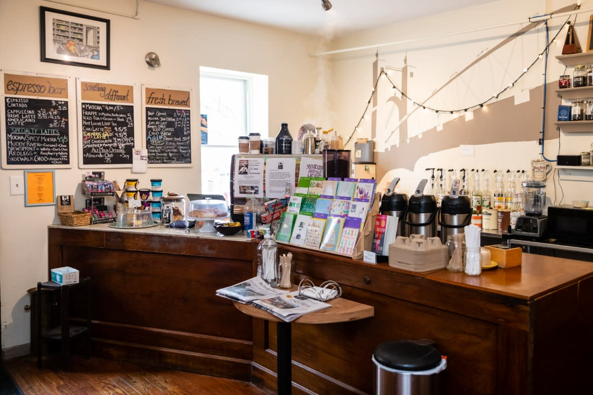 Inside counter of Roebling Books & Coffee with 3 chalk board menus on the left and a mural of the Roebling Bridge behind the counter.